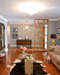 Living room with beige sofa, TV, wooden floor, cowhide rug, and a small dog. Decor includes flowers and framed photos.