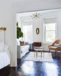A small bedroom that has a floating shelf stacked with books is connected to a living room