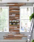 Rustic wood accent wall between two large windows, with hanging plants and a ladder leaning against the wall.