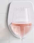 Wall-mounted wine glass holder with a glass of rosé against tiled background.