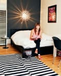 Woman sitting on bed with book, modern light fixture, striped rug, and wall art in cozy bedroom.