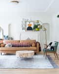 Living room with tan sofa, patterned pillows, gold floor lamp, plants, and a glass cabinet displaying cameras.