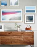 Mid-century modern sideboard with framed art, a black and gold lamp, and decor items including a vase and books.
