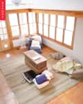 Sunroom with terracotta tiles, large windows, a ceiling fan, and a striped rug. Blue chair, wooden chest, and laundry basket.