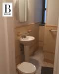 Small bathroom with beige tile walls, pedestal sink, and toilet under a mirrored cabinet.