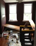 Room under renovation with dark walls, wooden planks, paint cans, and tools scattered on the floor.