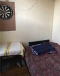 Small bedroom with a dartboard on the wall, a bed with patterned bedding, and a side table with a striped blanket.