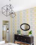 Geometric pendant light over dining area with patterned wallpaper, dark sideboard, and oval mirror.
