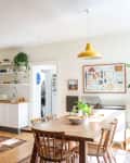 Bright kitchen with wooden countertops, open shelves, dining table, yellow pendant light, and green plant decor.