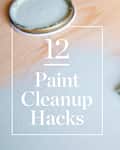 Paintbrush with white paint on wood surface, text overlay "12 Paint Cleanup Hacks."