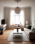 Living room with beige sofa, modern chandelier, coffee table, TV stand, and armchair by a window with sheer curtains.