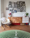 Mid-century modern living room with a wooden sideboard, gallery wall of black-and-white photos, and a green patterned rug.