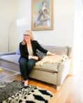 Woman sitting on a gray sofa with a small dog, next to a modern floor lamp and abstract painting.
