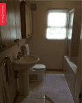 Small bathroom with pedestal sink, toilet, wooden cabinets, tiled floor, and window with blinds.