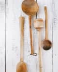 Four rustic wooden ladles of varying sizes on a white wooden surface.