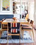 Dining room with wooden table, striped chairs, pendant light, and colorful wall art.