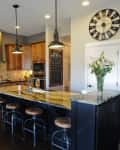 Spacious kitchen with wooden cabinets, granite island, bar stools, stainless steel fridge, and large wall clock.