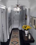 Hallway with chandelier, patterned runner, gray door, yellow flowers on table, and framed art on walls.