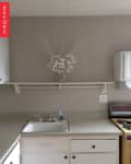 Simple kitchen with white cabinets, beige countertop, sink, and decorative white branches on a wall shelf.