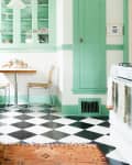 Mint green kitchen with checkered floor, white appliances, and a small dining table with two chairs.