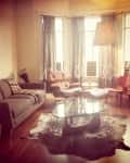 Cozy living room with a gray sofa, armchair, glass coffee table, and patterned curtains.