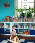 Child on wooden rocking horse in playroom with blue walls, bookshelves, and colorful books.