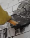 Applying black grout to white subway tiles with a trowel.