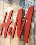 Red H&M logo on a glass storefront with blurred interior lights.
