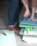 Man cutting blue wooden board with a utility knife, surrounded by tools and lumber, with "Before..." text.