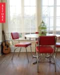 Dining area with red retro chairs, round table, green birdcage centerpiece, and a guitar by the window.