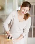 Woman cleaning a wooden kitchen counter with a sponge, near a black coffee maker and utensils.