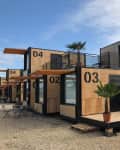 Stacked modular container homes with large windows, numbered 02 to 05, featuring small balconies and outdoor seating.