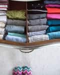 Drawer with neatly folded clothes in various colors and patterns, including stripes and polka dots, on a carpeted floor.