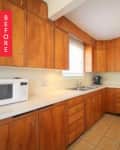 Wooden kitchen cabinets, white countertops, microwave, stove, and sink under a window with tiled floor.