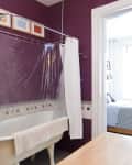 Clawfoot bathtub with shower curtain in a purple bathroom, adjacent to a bedroom with a patterned bedspread.