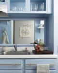 Blue kitchen with a sink, stove, and fridge. Countertop has a fruit basket. Art and photos decorate the walls and fridge.