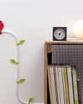 Decorative cable clips shaped like leaves and a red bird on a wall, next to a shelf with books and a clock.