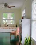 Sunroom with daybed, floral cushions, two vintage chairs, large mirror, ceiling fan, and potted plant by the window.