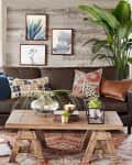 Living room with brown leather sofa, patterned pillows, wooden coffee table, large plant, and framed botanical art.