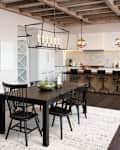Modern kitchen and dining area with black table, six chairs, pendant lights, and a bar with stools.