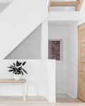 Wooden bench with potted plant under a modern staircase in a minimalist room.