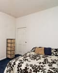 Small bedroom with floral bedspread, blue carpet, and a tall dresser beside a closed white door.