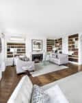 Spacious living room with built-in bookshelves, two gray sofas, a fireplace, and a glass coffee table on a hardwood floor.