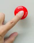 Finger pressing a red reset button on a light surface.