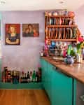 Colorful kitchen with turquoise cabinets, wooden countertops, dish rack, paintings, and flowers in a vase.