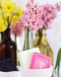 Colorful soap bars in a white dish with yellow daffodils and pink hyacinths in the background.