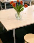Vase with orange tulips on a light wood table, next to a matching stool.
