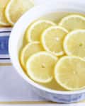 Lemon slices floating in a white bowl of water on a striped cloth.