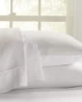 Two stacked white pillows on a bed with a window in the background.