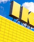 Large yellow IKEA sign on a building with a grid pattern against a blue sky with clouds.